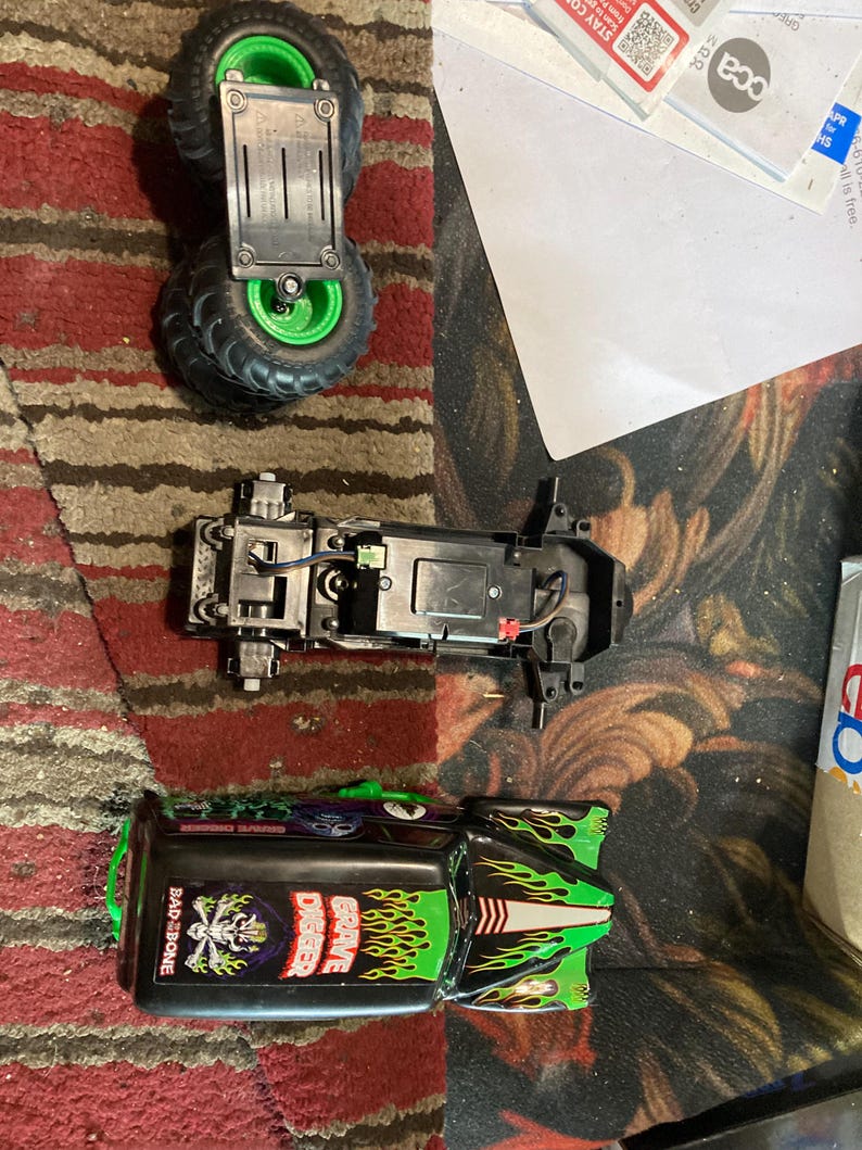 May include: A disassembled toy monster truck with green and black paint. The truck is labeled "Grave Digger" and "Bad to the Bone".
