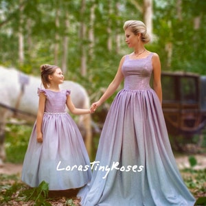 Könnte beinhalten: Eine Mutter und ihre Tochter tragen passende Ombre-Kleider in Lila und Blau. Die Kleider haben eine glitzernde Textur und sind bodenlang. Das Kleid der Mutter hat einen quadratischen Ausschnitt und das Kleid der Tochter einen Rüschenausschnitt. Der Text "LorastinyRoses" ist im Bild sichtbar.