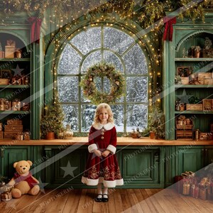 May include: A young girl in a red velvet dress with white trim stands in front of a large window with a snowy scene. The room is decorated for Christmas with a wreath, lights, and a teddy bear.