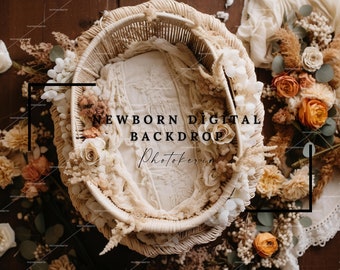 Op de afbeelding: Een witte rieten mand gevuld met witte stof en gedroogde bloemen, met de tekst "NEWBORN DIGITAL BACKDROP Photokerin" op de stof. De mand is omringd door gedroogde bloemen en groen.
