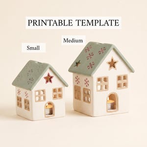 Peut inclure: Deux bougeoirs en forme de maison étiquetés comme modèle imprimable, avec une petite et une moyenne taille. Les maisons sont blanches avec des toits vert sauge, dotées de fenêtres découpées, d'ouvertures en étoile et de flocons rouges sur le toit.