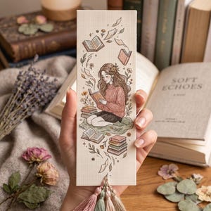 May include: A rectangular bookmark with a cross-stitch design. The illustration depicts a person reading, surrounded by books and floral elements. The bookmark has a tassel with pink, green, and beige threads.