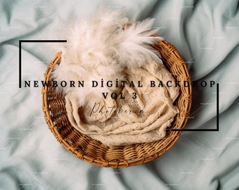 Op de afbeelding: Een rieten mand met een beige stof en witte veren erin, op een lichtblauwe achtergrond. De tekst "NEWBORN DIGITAL BACKDROP VOL 3" is zichtbaar.