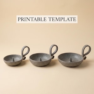 May include: Three speckled gray ceramic candle holders with loop handles. Each holder has a small spike in the center for securing a candle. The text "PRINTABLE TEMPLATE" is above the candle holders.