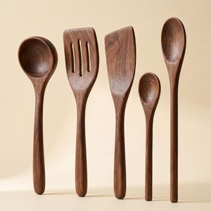 May include: A set of five wooden kitchen utensils, including a ladle, slotted spatula, solid spatula, small spoon, and a serving spoon. The utensils are made of dark brown wood and are arranged against a neutral background.