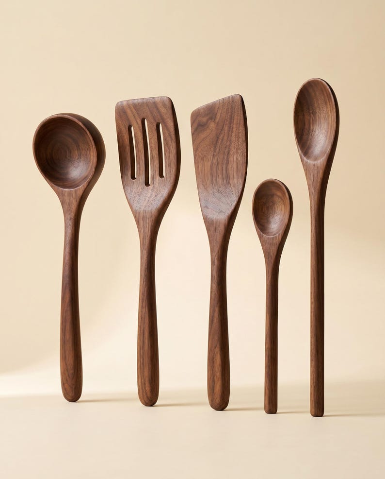 May include: A set of five wooden kitchen utensils, including a ladle, slotted spatula, solid spatula, small spoon, and a serving spoon. The utensils are made of dark brown wood and are arranged against a neutral background.