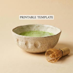 May include: A speckled ceramic bowl filled with green matcha tea, next to a bamboo matcha whisk. The bowl has a textured surface and a unique shape. The text "PRINTABLE TEMPLATE" is displayed above the bowl.
