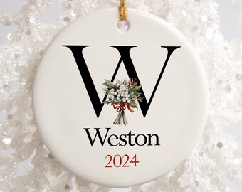 Puede incluir: Adorno navideño de cerámica blanca con una letra W negra y un ramo de flores dentro de la letra. El adorno también tiene el nombre Weston y el año 2024 impreso.
