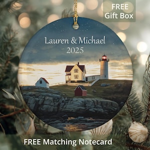 May include: A round ceramic ornament featuring a coastal scene with a lighthouse, house, and text that reads "Lauren & Michael 2025." The ornament has a gold-colored hanging loop and the words "FREE Gift Box" and "FREE Matching Notecard" are also visible.