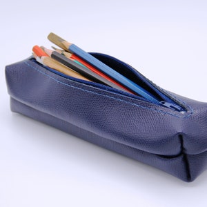 May include: A blue leather pencil case with a zipper closure. The case is open and filled with pencils and pens.