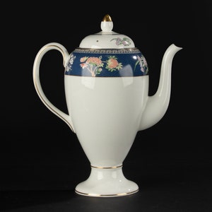 Op de afbeelding: Witte porseleinen theepot met een gouden rand en een blauw en bloemmotief. De theepot heeft een deksel met een gouden knop.