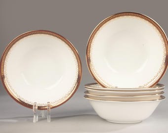May include: A set of white ceramic bowls featuring a wide, dark brown rim decorated with a repeating gold geometric pattern. One bowl is displayed upright on a clear stand, while four additional bowls are stacked neatly in a vertical column.