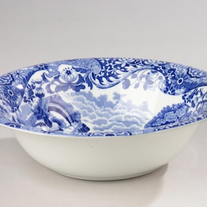 May include: A white ceramic bowl with a blue floral pattern around the rim and inside. The bowl has a wide, shallow shape, suitable for serving food. The blue design features flowers and foliage.