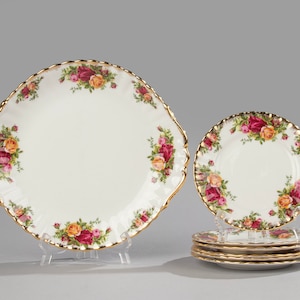 Puede incluir: Un juego de platos de porcelana blanca con borde dorado y diseño floral. El juego incluye un plato ovalado grande para servir y seis platos redondos más pequeños.