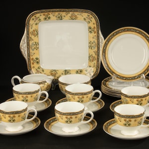 May include: A porcelain tea set featuring a square serving platter, six teacups, six saucers, a creamer, and a sugar bowl. Each piece has a white centre, a yellow border with a floral pattern, and a black and gold decorative rim trim.