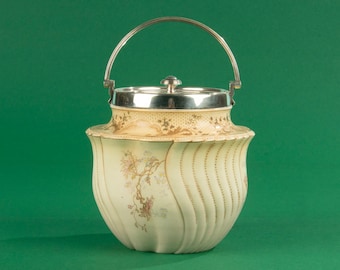 May include: A white ceramic cookie jar with a silver lid and handle. The jar has a floral design and a wavy, ribbed pattern.