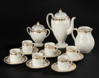 May include: A white porcelain tea set with gold accents. The set includes a teapot, creamer, sugar bowl, and six cups and saucers.