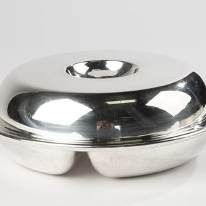 May include: A shiny, silver serving dish with a lid. The dish has a round, shallow base with three compartments and a matching lid with a central handle. The reflective surface of the dish creates a bright, clean look, suitable for serving food.