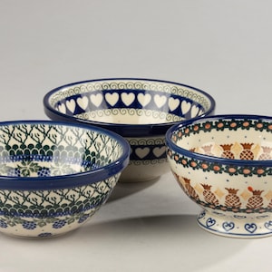 Op de afbeelding: Drie keramische kommen met blauwe randen en ingewikkelde patronen. De kommen hebben ontwerpen van harten, ananassen en bloemmotieven in blauwe, groene en bruine tinten. De kommen variëren in grootte en vorm.