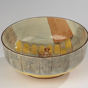 May include: A decorative ceramic bowl with a light blue interior and exterior. The bowl features a brown rim and a yellow base. The interior design includes a figure and arched windows with a brown roof.