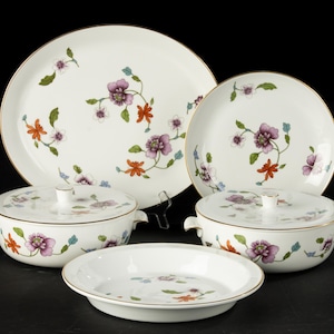 May include: A set of five white porcelain dishes featuring a floral design in shades of purple, orange, and green. The set includes a large oval platter, a round serving dish, two covered casserole dishes, and a smaller round dish.