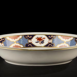 Può includere: Ciotola ovale in ceramica bianco sporco con bordo decorativo. Il bordo presenta un motivo ripetuto di accenti blu, pesca e oro. Un motivo floreale è centrato all'interno. La ciotola ha un bordo dorato.