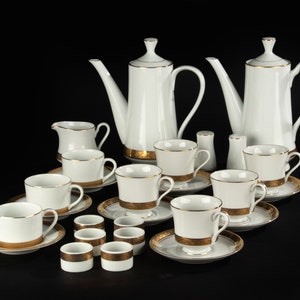 Op de afbeelding: Een wit porseleinen theeservies met gouden rand. De set bevat een theepot, een roomkan, een suikerpot, zes kopjes en zes schoteltjes.