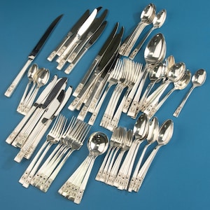 May include: A large collection of polished silver-tone stainless steel flatware, including various knives, forks, and spoons. Each piece features a vertical ribbed handle design with a decorative textured band near the base of the utensil.