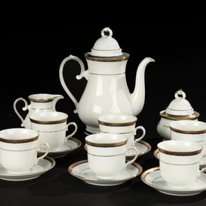 Puede incluir: Un juego de té de porcelana blanca con ribetes dorados y azules. El juego incluye una tetera, una jarra de crema, un azucarero y seis tazas y platillos.