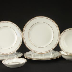 Op de afbeelding: Een set wit keramieken servies met een verfijnde grijze en gouden patroonrand. De set bevat diverse dinerborden, saladeborden en kleine kommen, allemaal afgewerkt met een dunne gouden rand langs de buitenkant van elk onderdeel.
