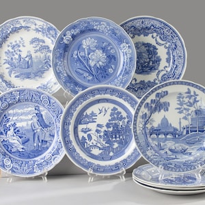 Op de afbeelding: Een verzameling van zes ronde keramische borden met blauw-witte transferware patronen. De ontwerpen bevatten diverse pastorale scènes, architecturale landschappen en florale motieven met gedetailleerde randen op een witte achtergrond.