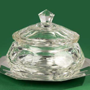 May include: A clear glass sugar bowl with a lid and a silver base. The bowl and lid are faceted and have a geometric design.