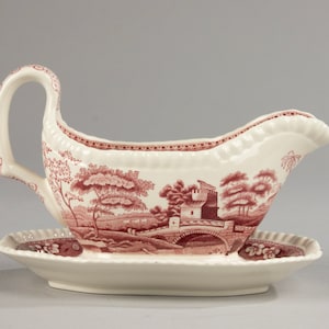 May include: A white porcelain gravy boat with a red and white floral pattern. The boat has a handle and a matching saucer.