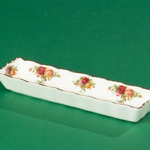 Puede incluir: Un plato rectangular blanco para servir con un borde dorado y un patrón floral con rosas rojas, amarillas y verdes.