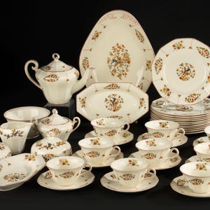 May include: A complete vintage porcelain tea set with floral and foliage designs. The set includes a teapot, serving platters, cups, saucers, sugar bowl, creamer, and plates. The set is cream-colored with brown and red accents.
