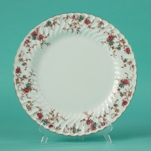 Op de afbeelding: Witte keramische dinerbord met een gouden rand en een bloemenpatroon in roze, blauwe en bruine tinten.