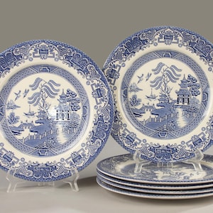 Puede incluir: Una taza de cerámica blanca con un asa negra y el texto "But First, Coffee" en negrita negra. La taza se encuentra sobre un fondo borroso, sugiriendo un ambiente acogedor.