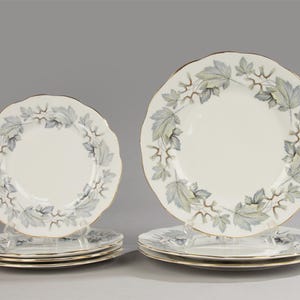 Pode incluir: Conjunto de seis pratos de jantar de porcelana branca com borda dourada e design de folhas cinzas e verdes.