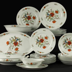 Op de afbeelding: Een compleet wit porseleinen servies met een kleurrijk vogel- en bloemmotief. De set bevat borden, kommen, een serveerschaal, een dekselschaal en een sauskom. De vogel heeft blauwe, gele en groene veren, met rode bloemen.