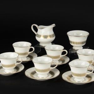 Puede incluir: Un juego de té de porcelana blanca con ribetes dorados y verdes. El juego incluye una jarra de crema, un azucarero y seis tazas de té y platillos.