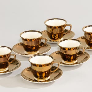 Op de afbeelding: Set van zes gouden theekopjes en schoteltjes met een metallic gouden afwerking. De kopjes en schoteltjes hebben een witte binnenkant.