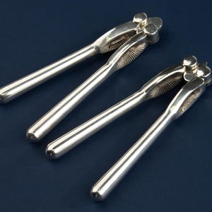 Peut inclure: Quatre casse-noix argentés sur une surface bleu foncé. Chaque casse-noix a un long manche lisse et une tête décorative avec un motif floral. Les casse-noix sont en métal brillant et réfléchissant. Les manches mesurent environ 15 cm de long.