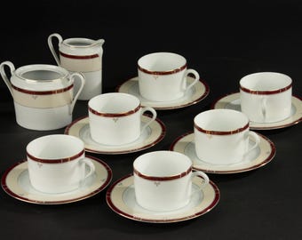 May include: A white porcelain tea set with a cream and burgundy border. The set includes cups, saucers, a creamer, and a sugar bowl. The cups and saucers have a simple, elegant design, perfect for serving tea or coffee.