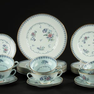 Puede incluir: Un juego de vajilla de porcelana completo con platos, platillos y cuencos de sopa. Las piezas blancas tienen un diseño floral azul con ribete dorado. El juego incluye platos llanos, platos de ensalada, cuencos de sopa y platillos.
