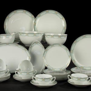 May include: A set of white porcelain dinnerware with a green and gold floral pattern. The set includes plates, bowls, and cups.