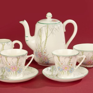 May include: A vintage porcelain tea set with a teapot, creamer, sugar bowl, two teacups, and saucers. The set features a floral design with pink, blue, and yellow flowers, and green accents on a white background.