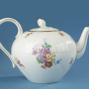 Op de afbeelding: Een witte porseleinen theepot met een delicaat reliëf spiraalpatroon en handgeschilderde bloemenboeketten in paars, rood, geel en blauw. De theepot heeft een bijpassend deksel met een knop en gouden accenten op het handvat en de rand.