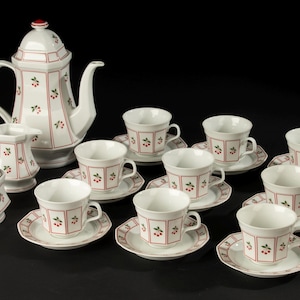 Puede incluir: Juego de té de cerámica blanca con un patrón de cerezas rojas. El juego incluye una cafetera, una cremera, un azucarero y varias tazas y platillos. El diseño presenta ribetes rojos y motivos de cerezas.