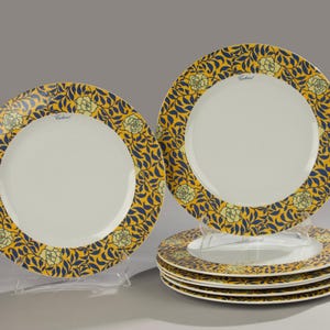Può includere: Un set di sei piatti in ceramica bianca con un bordo floreale decorativo giallo e blu navy. I piatti hanno un centro bianco e sono esposti su supporti in plastica trasparente. I piatti fanno parte di un set di stoviglie.