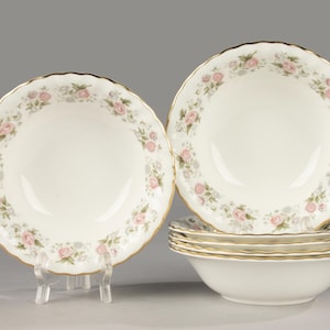 May include: A collection of white porcelain bowls featuring a floral design of pink roses and green foliage. Each bowl has a scalloped edge with gold trim. The set comprises six bowls.